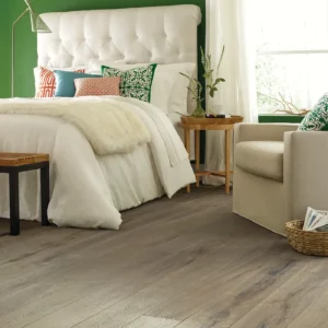 Gray-toned hardwood in a bedroom with a white tufted headboard | Broadway Carpet & Flooring